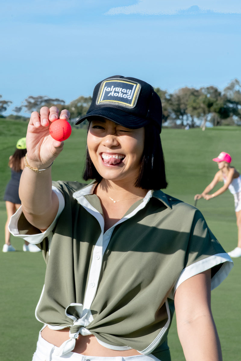 Load image into Gallery viewer, Model wearing black Fairway Stoked golf trucker hat  on a golf course holding a golf ball.

