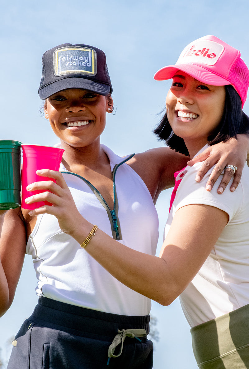 Load image into Gallery viewer, Two model cheers-ing with cups.  One is wearing a black Fairway Stoked golf  trucker hat and the other is wearing a Hot Pink Pirdie golf trucker hat.
